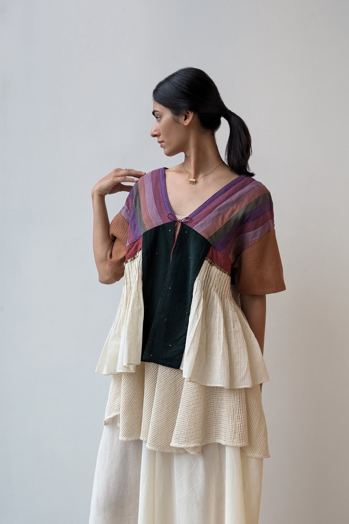 Woman wearing a layered outfit with a colorful top and beige skirt against a plain background