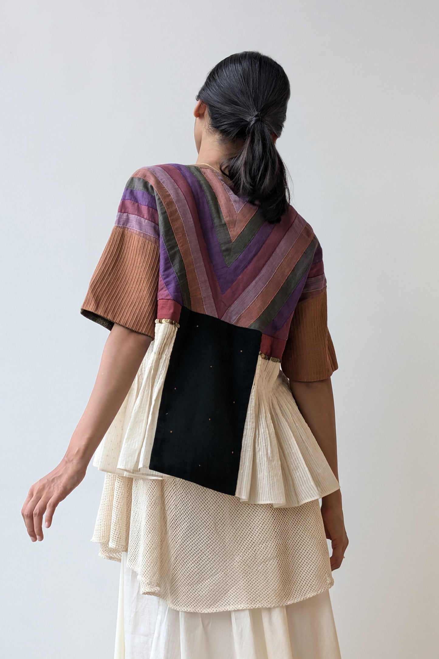 Person wearing a colorful top and layered skirt against a plain background