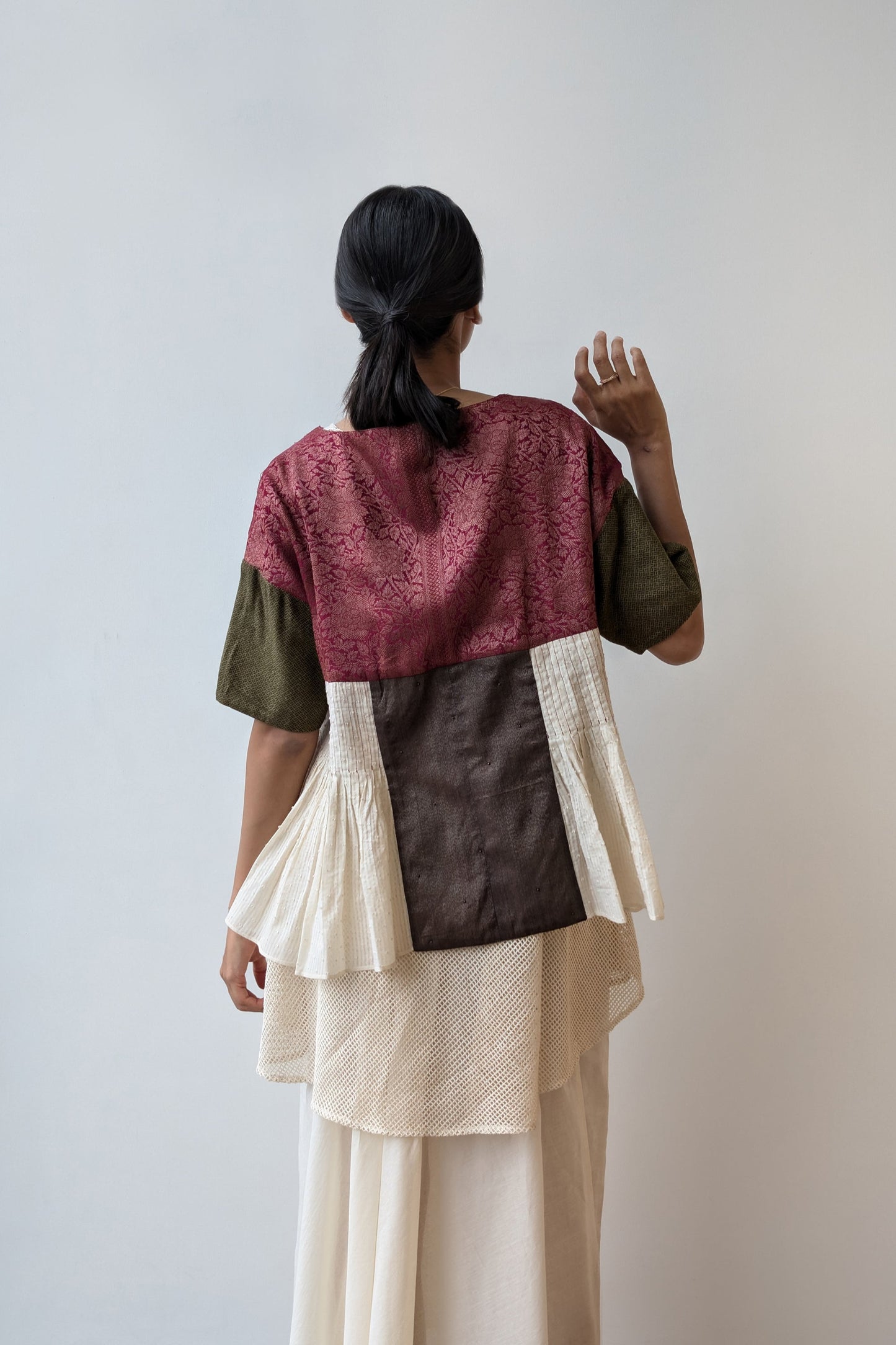 Person wearing a reversible layered outfit with a maroon top, green sleeves, brown middle section, and beige bottom against a white wall. For Diwali.