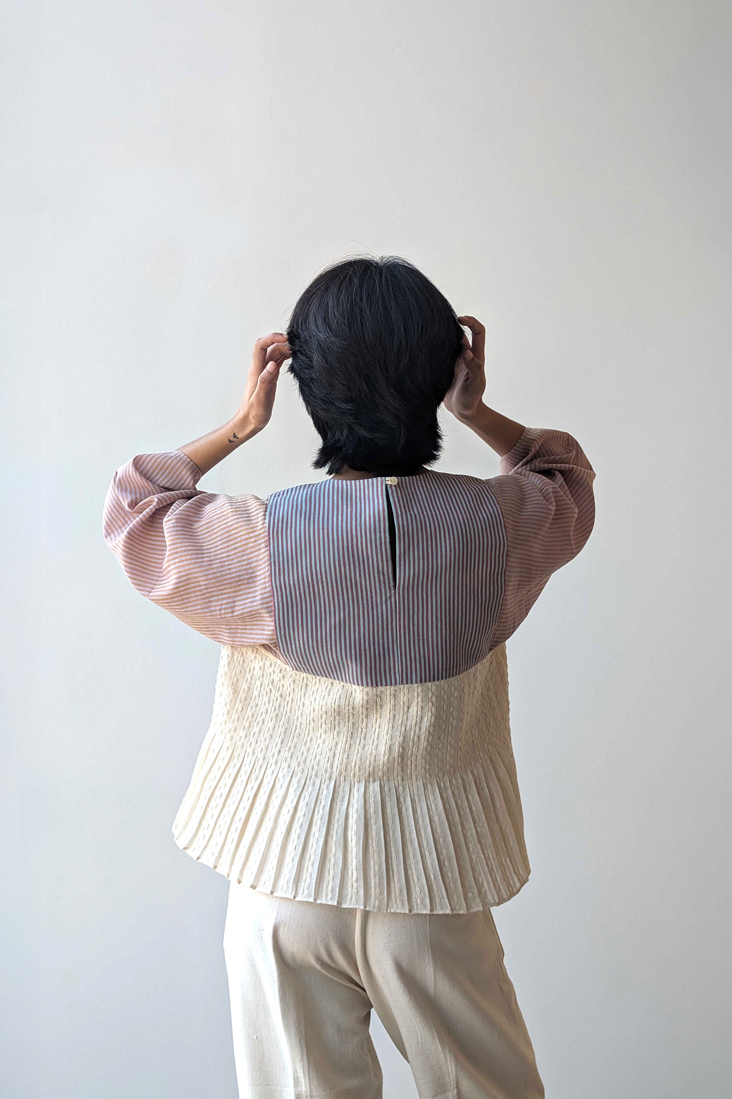 Person wearing a upcycled reversible pleated top, striped shirt, and beige pants against a plain background for Diwali & festive occasions.