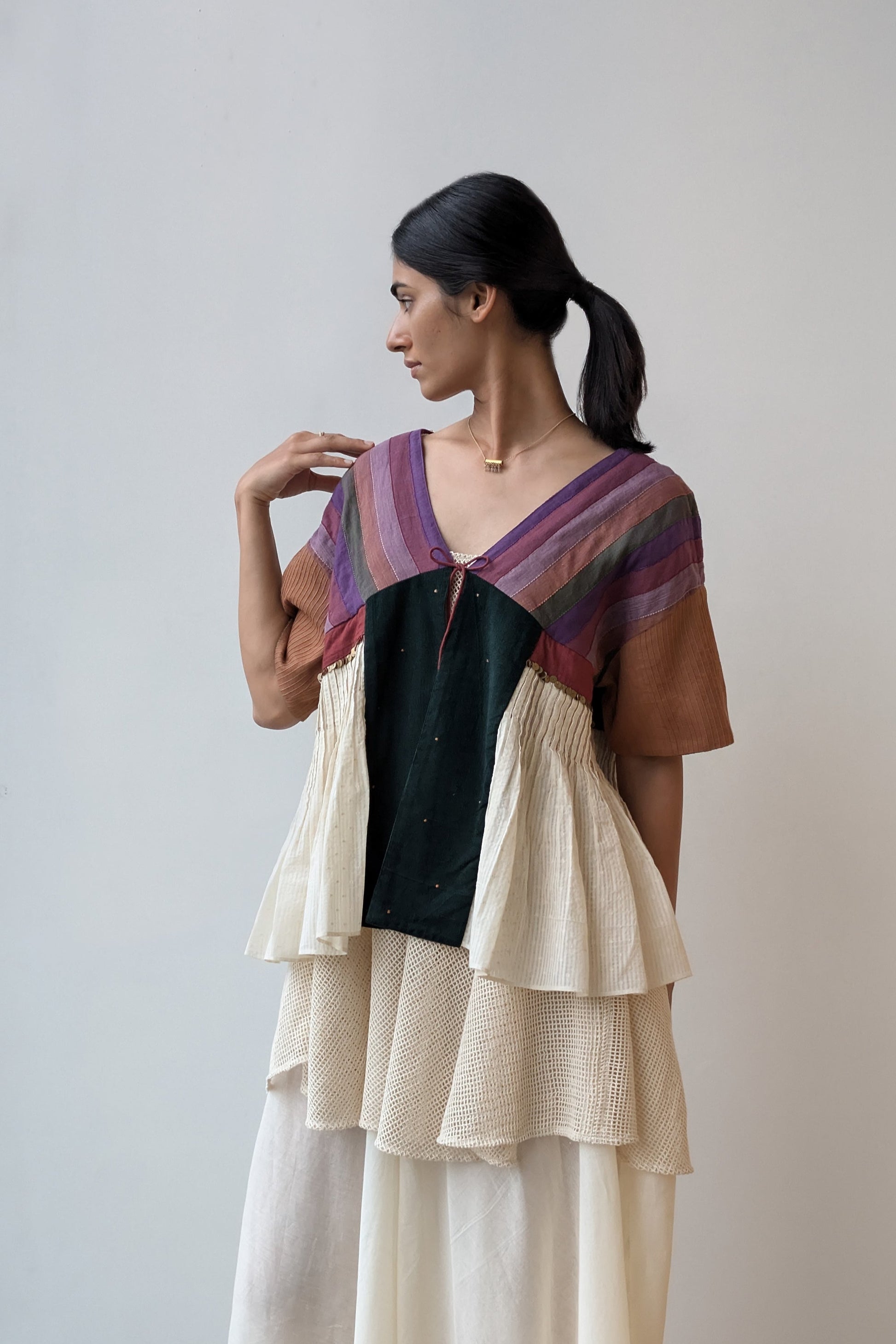 Woman wearing a layered outfit with a colorful top and beige skirt against a plain background