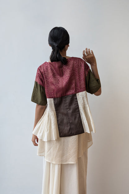 Person wearing a reversible layered outfit with a maroon top, green sleeves, brown middle section, and beige bottom against a white wall. For Diwali. 
